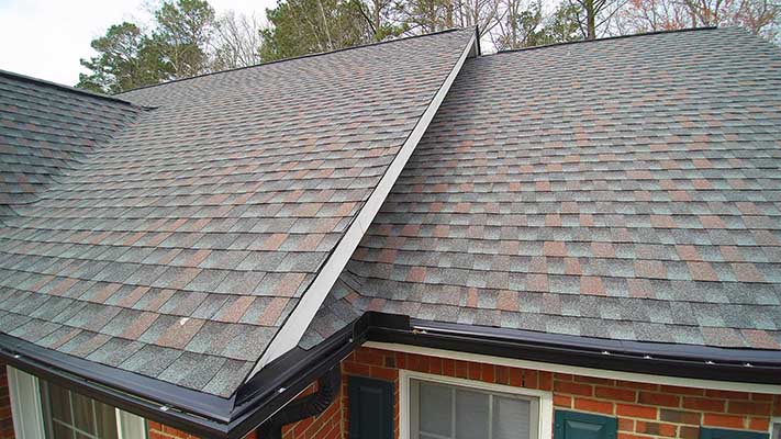 A roof with multiple colors of shingles and a gutter.
