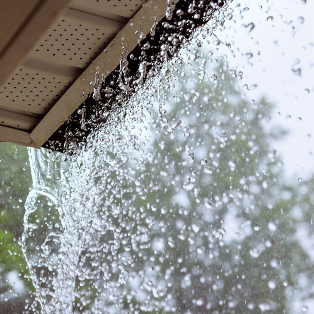 Clear water cascades from a clogged, overflowing house gutter during a rain shower.