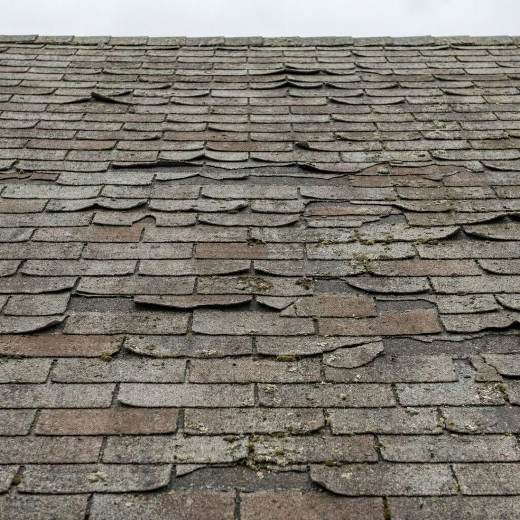 An aged residential roof showing signs of curling shingles, indicating it may be time for a replacement.