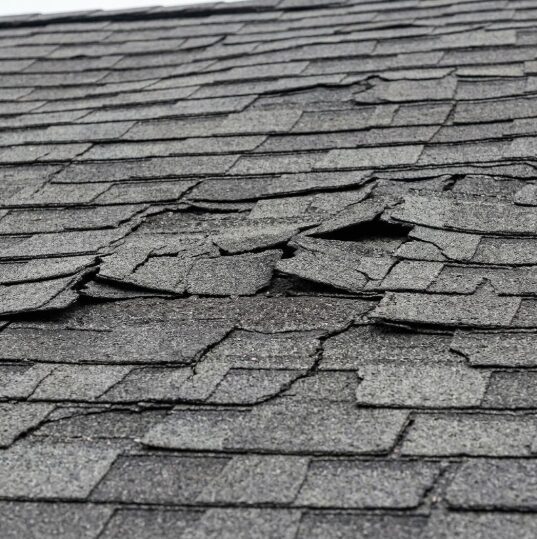A close-up view of severely damaged and missing roof shingles.