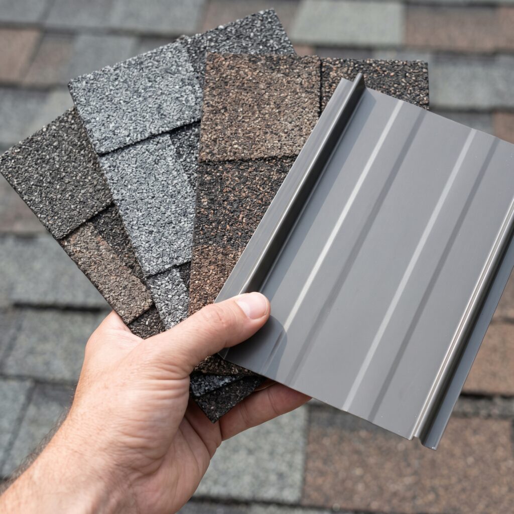 A hand compares various asphalt shingle samples and a metal roofing panel.
